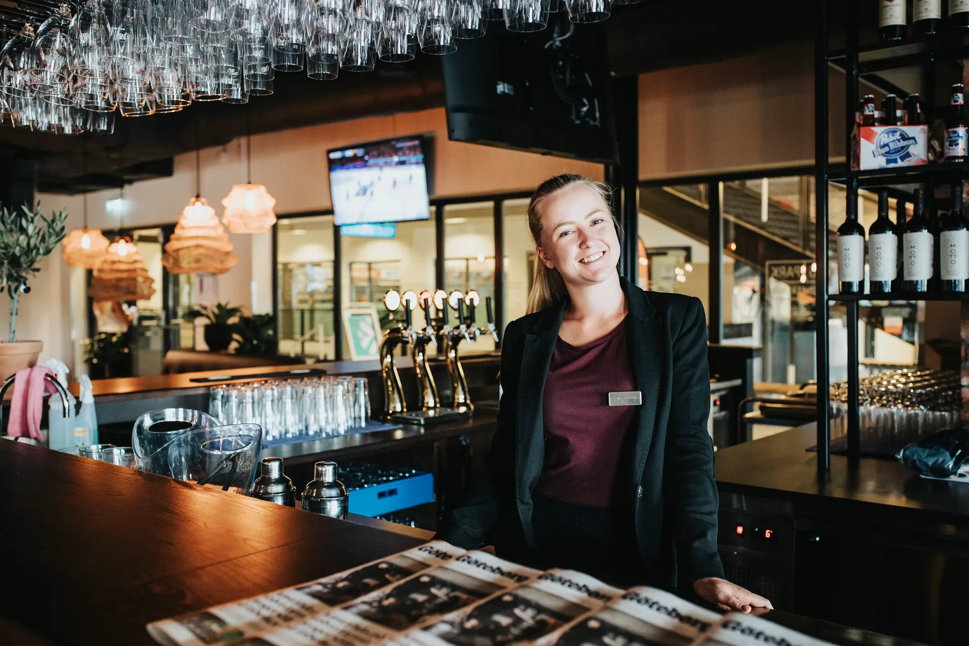Restaurang med rutig duk, padelracketar och spårvagn utanför fönstret.